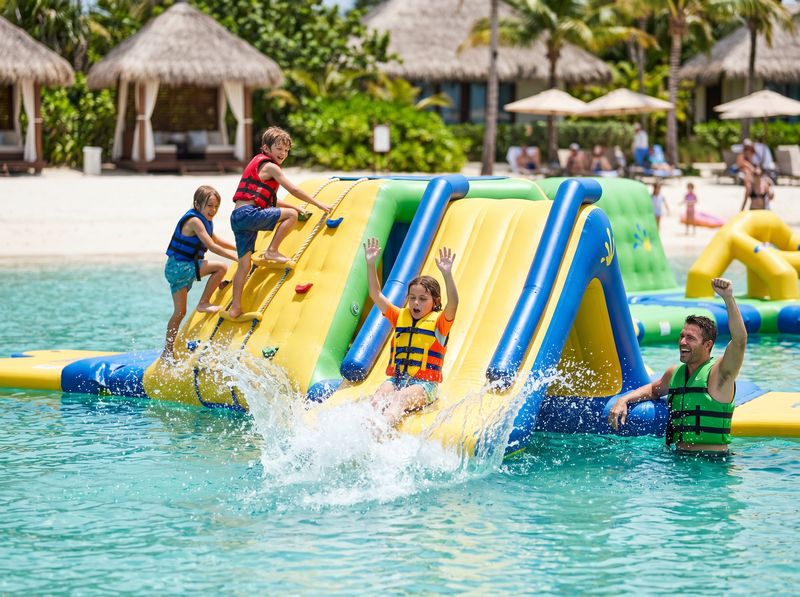 Kids and parents on a floating inflatable water playground with slides on a crystal lagoon